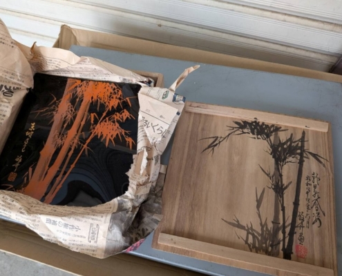 黒漆に朱色で竹文様が描かれた漆器と、墨絵で竹が描かれた共箱を並べたイメージ画像｜漆器の文化的背景と市場価値を表現