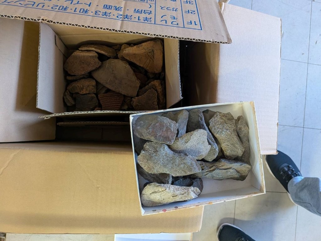 段ボール箱に分けて保管されていた石斧と縄文土器片を仕分けしながら査定する考古資料整理の現場