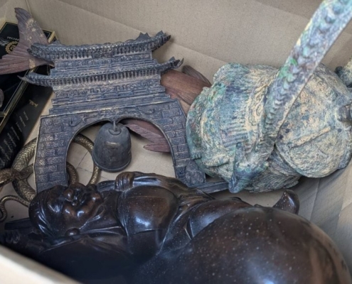 段ボール内にまとめられた金属製置物一式(楼門風の飾りと人物像、緑青の出た金属器が見える)