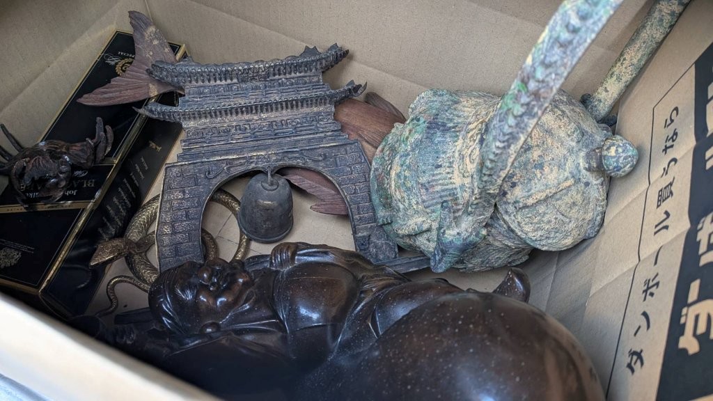 段ボール内にまとめられた金属製置物一式（楼門風の飾りと人物像、緑青の出た金属器が見える）