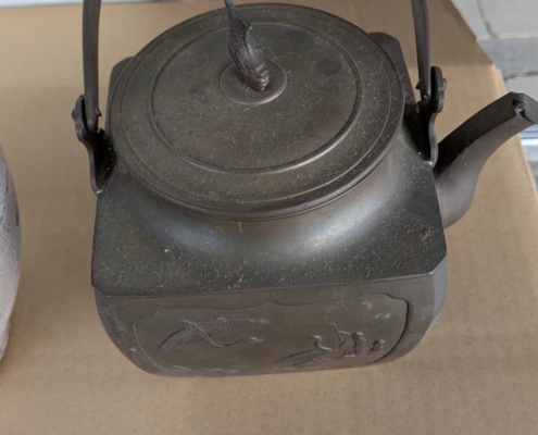 角胴の青銅製茶瓶（湯沸形）の正面全体。持ち手と注ぎ口、胴面の鶴文様浮彫が確認できる