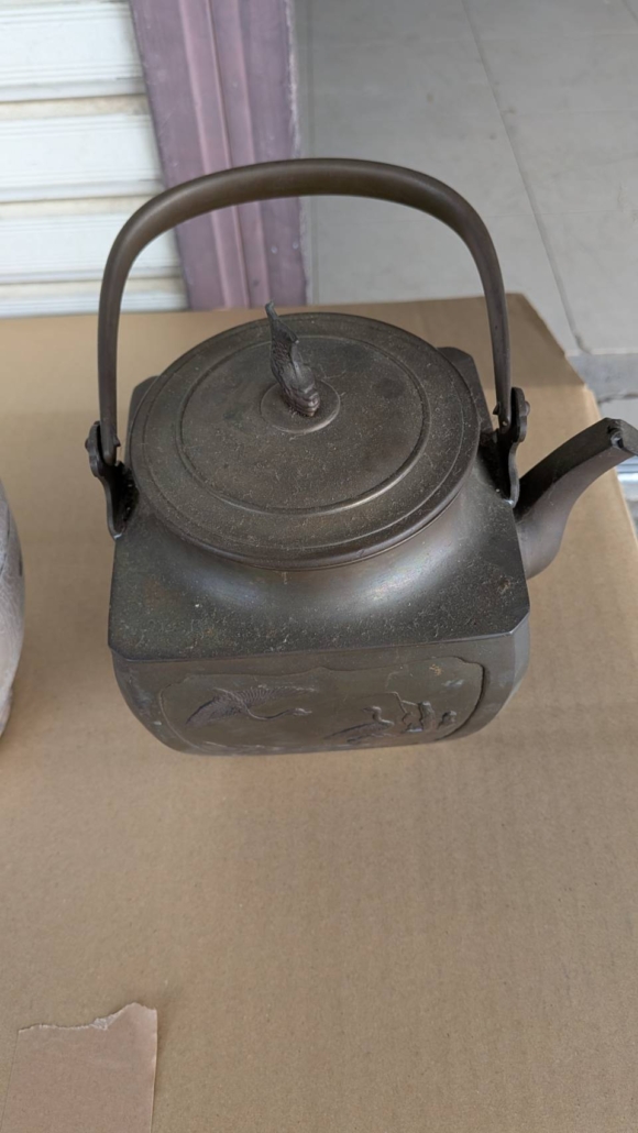 角胴の青銅製茶瓶（湯沸形）の正面全体。持ち手と注ぎ口、胴面の鶴文様浮彫が確認できる